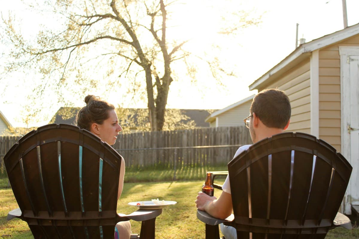 Two neighbors talking in lawn chairs in a backyard